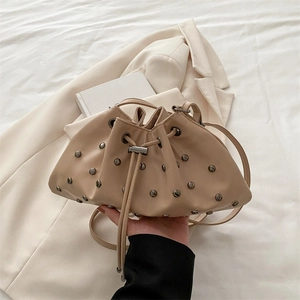 Minimalist beige drawstring bucket bag with metal rivet accents and crossbody strap