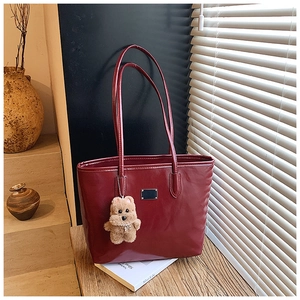 Primer plano del bolso tote de cuero burdeos con etiqueta metálica y colgante de osito
