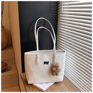 Detail view of white faux leather tote bag with a cute brown plush bear charm