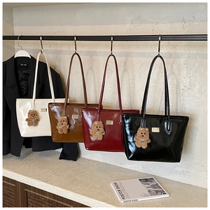 Detail of glossy leather tote bags with metal plaque and plush bear charms in four colors