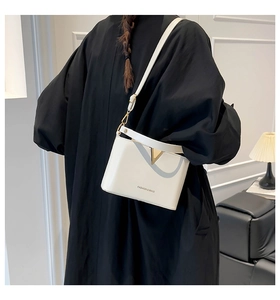 Detailed shot of a white leather bucket bag with a golden V-shaped metal clasp on a model
