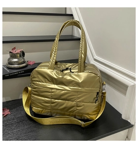 Detail of a gold quilted puffer crossbody bag featuring shiny metallic fabric and a wide strap