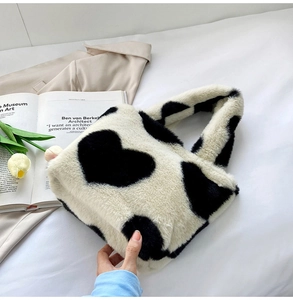 Gros plan du sac à main en peluche avec motif de vache à cœur noir et blanc sur lit