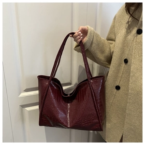 Close-up of burgundy crocodile pattern tote bag held by a model in a beige coat