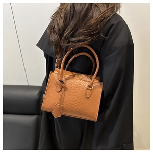 Detail of a brown crocodile pattern tote bag featuring golden hardware and a top handle