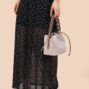 Detail of grey bucket bag with brown chain link handle and woven leather texture