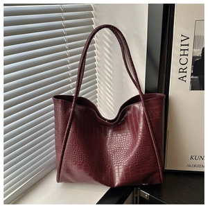Detail of the crocodile pattern texture and glossy finish on the deep red tote bag