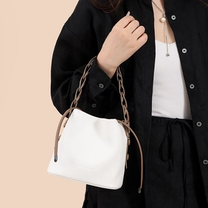 Detail of white bucket bag featuring brown chain handle and lychee grain leather texture