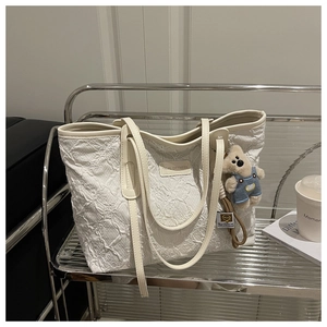 Dettaglio della borsa tote bianca ricamata con ciondolo a orsetto e patch in pelle