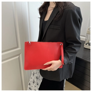 Detail of red leather envelope clutch bag with silver zipper and wrist strap on model