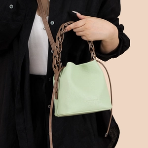 Detail of mint green woven bucket bag with leather texture and brown chain handle