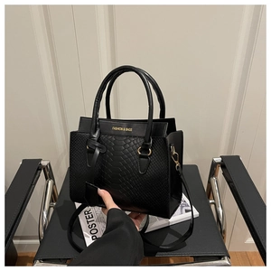 Detail of black crocodile texture handbag with gold hardware on a modern leather chair