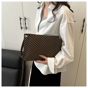 Model holding a large dark brown envelope clutch bag with vintage monogram patterns