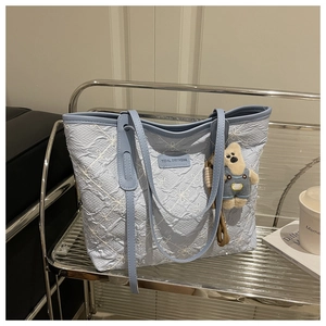 Dettaglio della borsa tote azzurra con ricamo floreale e ciondolo orsetto di peluche