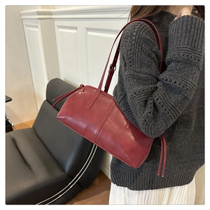 Detail of burgundy baguette shoulder bag with long drawstring side tassels on a model
