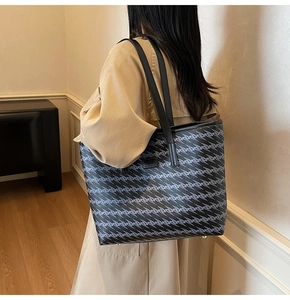 Detail showing metal feet and textured wave pattern on a large black tote bag