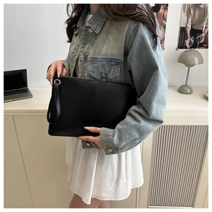 Minimalist black matte leather envelope clutch bag held by model in office setting