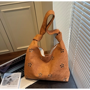 Détail du design floral ajouré et de la bandoulière nouée sur un sac cabas en daim brun