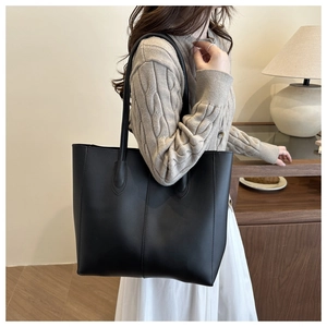Detail of a minimalist black leather tote bag worn with a cozy beige knit sweater