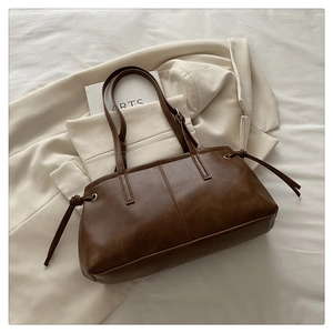 Deep coffee vintage tote bag with side drawstring knots placed on a blazer and book