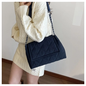Detail of navy blue quilted oxford fabric cross-body bag with silver chain strap worn on person