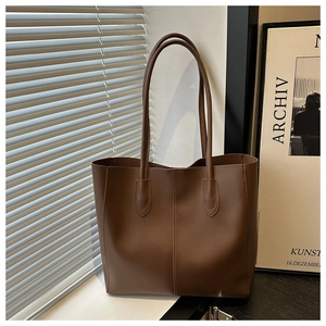 Detail of a large brown leather tote bag with vertical stitching in a modern interior setting