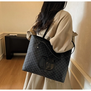 Détail du grand sac cabas avec imprimé M et logo en relief porté à l'épaule par un mannequin
