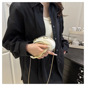 Close-up of a white patent leather semicircular crossbody bag with a gold metal ring handle
