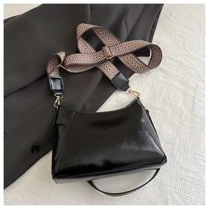 Nahaufnahme der schwarzen Lackledertasche mit braunem Hahnentritt-Gurt und goldenen Beschlägen