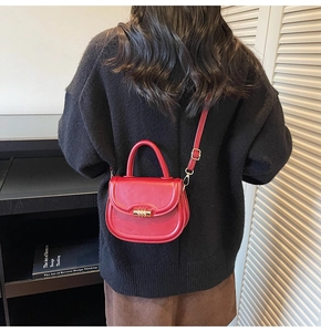 Model view of a red semi-circular saddle bag worn with a black sweater and leather strap
