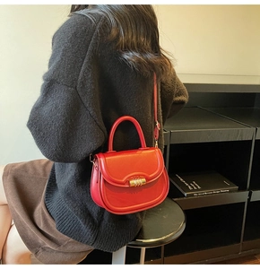 Detail of red saddle bag featuring a gold cylindrical lock and a detachable shoulder strap