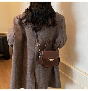 Brown faux leather saddle bag worn over a grey vintage blazer in a minimalist indoor setting