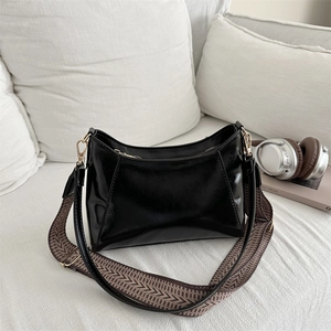 Schwarze glänzende Schultertasche mit gemustertem breitem Riemen auf Sofakissen