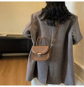 Close-up of brown saddle bag with gold metal buckle on grey tweed blazer background