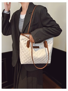 Detail of white quilted tote bag with brown leather handles and fashion logo plaque