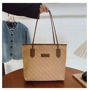 Detail of khaki quilted tote bag with diamond pattern and brown leather straps