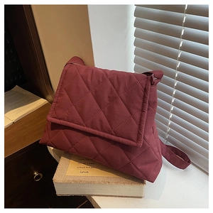 Close-up of wine red quilted nylon crossbody bag with bubble texture on white desk