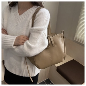 Détail d'un sac cabas en cuir grainé kaki avec de fines anses porté sur un pull blanc chic