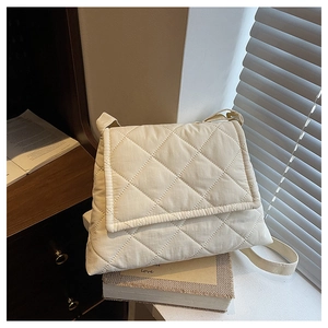Detailed view of cream quilted crossbody bag with rhombic stitching on a wooden desk