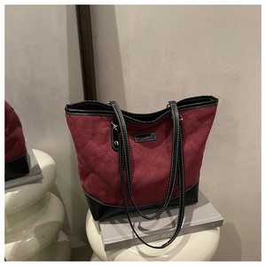 Detail of burgundy quilted tote bag with contrast stitching on black leather straps