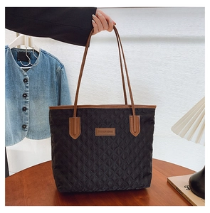 Detail of black quilted tote bag with brown leather handles and fashion logo patch