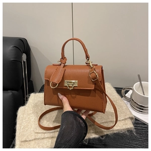 Detail der karamellfarbenen Handtasche mit Lychee-Maserung und goldener Schnalle auf Decke