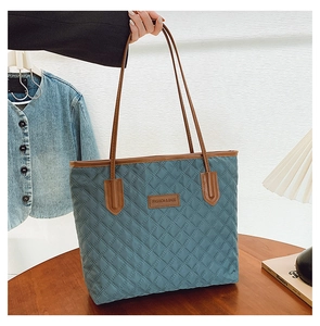 Detail of blue quilted tote bag featuring a leather logo patch and brown shoulder straps