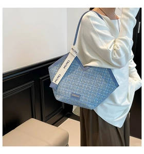 Detail of blue tweed tote bag showing fashion tag and white lettered shoulder strap