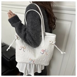 Detail of white tote bag featuring embroidered bows and quilted letter E textures on shoulder
