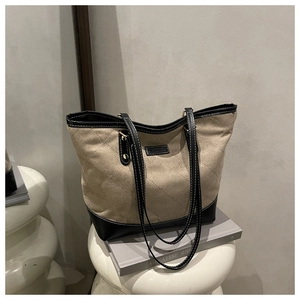 Close-up of beige canvas tote bag with black quilted leather pocket and fashion label