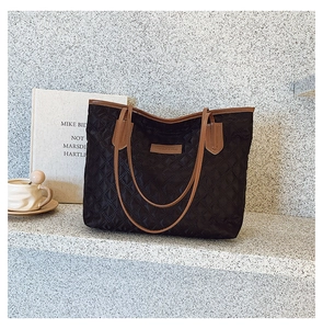Detail of black quilted tote bag with brown leather trim and logo patch on desk