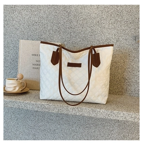 Close-up of white quilted tote bag with brown straps on a minimalist stone surface