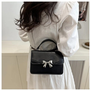 Fashionable black crossbody bag with silver metal bow worn by model on white dress
