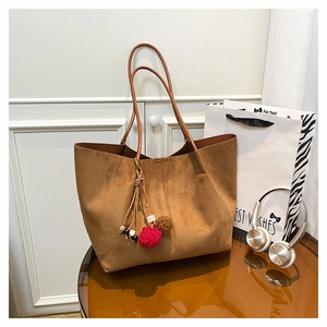 Detail of a large brown suede tote bag with colorful ethnic pompom charms and thin straps